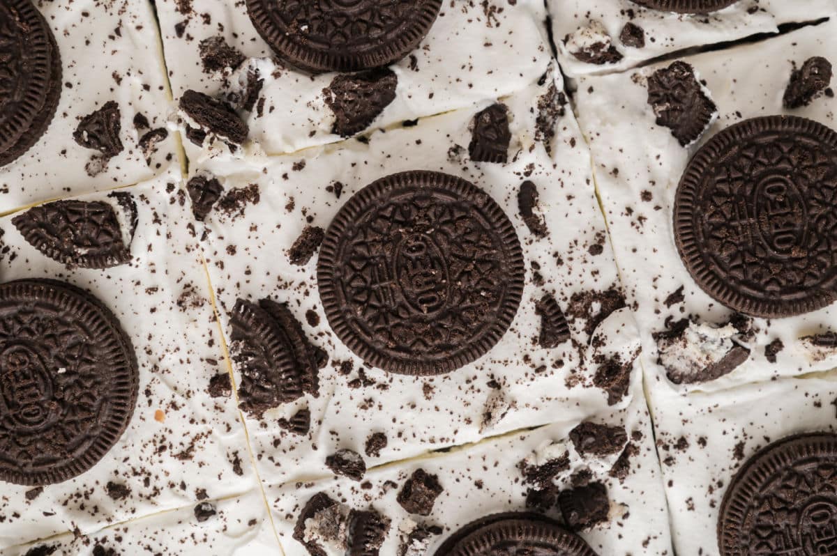 Close-up of dessert bars topped with whole and crumbled chocolate sandwich cookies on a layer of white frosting, arranged in a grid pattern, reminiscent of an Oreo poke cake.