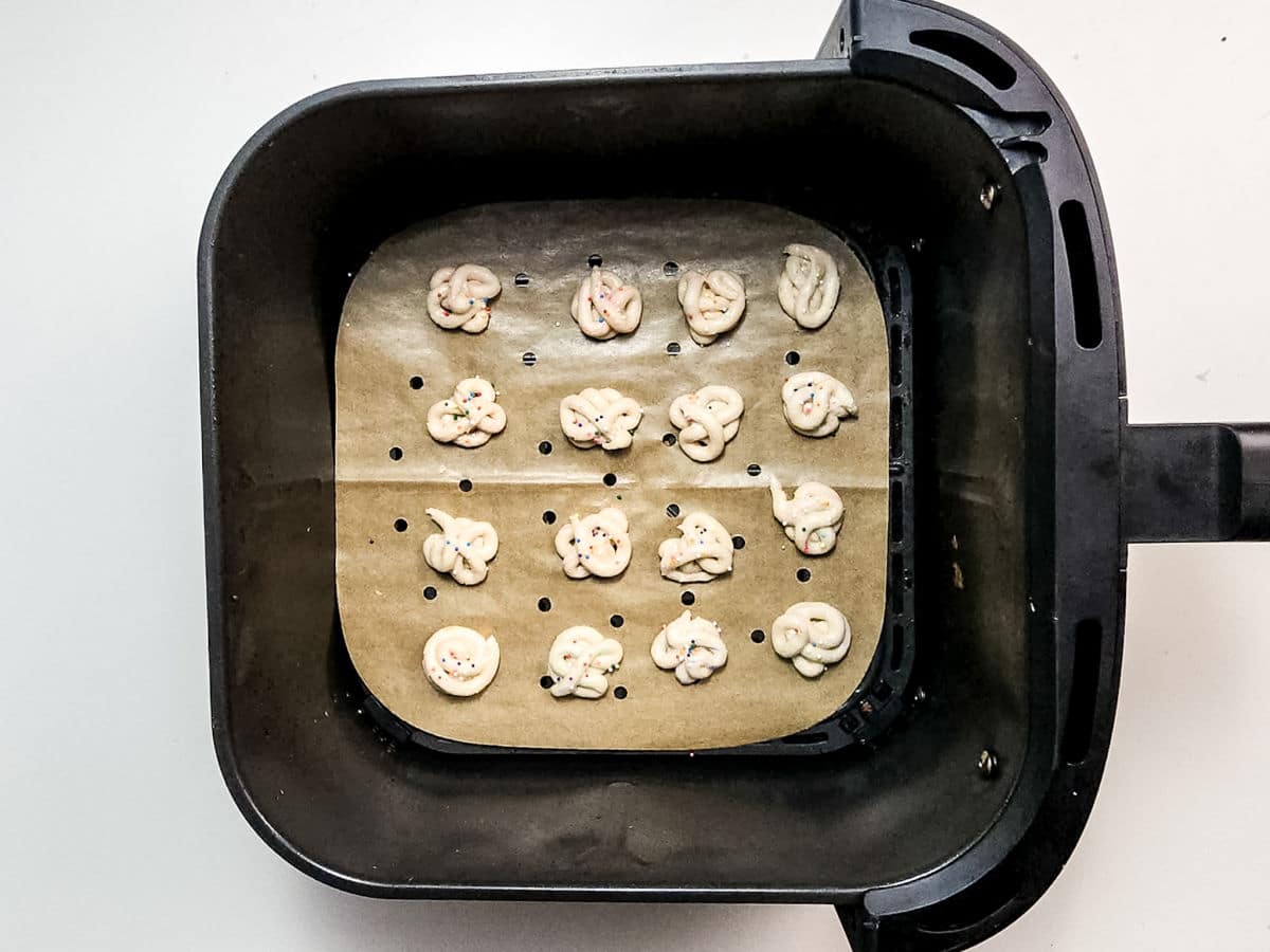 Overhead view of small pretzel-shaped dough pieces on parchment paper inside an air fryer basket, ready to be baked, reminiscent of Air Fryer Funnel Cake Bites.