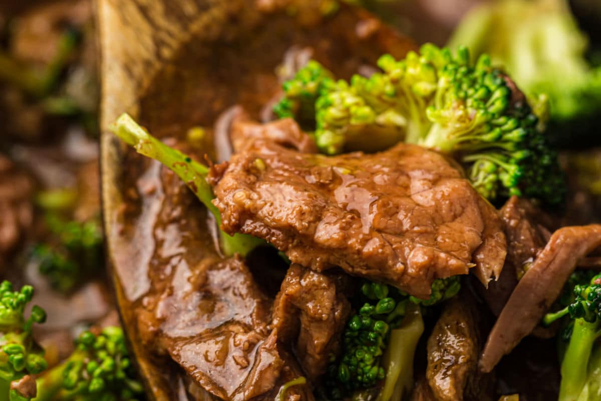 Close-up of beef and broccoli slow cooker stir-fry, showing tender beef slices coated in sauce, bright green broccoli florets, and a wooden spoon mixing the ingredients.