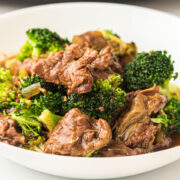 A close-up of a white bowl filled with beef and broccoli slow cooker stir-fry, featuring tender slices of beef and green broccoli florets coated in a savory brown sauce.