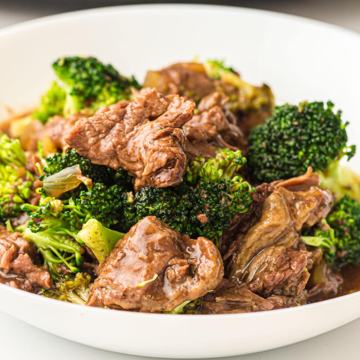A close-up of a white bowl filled with beef and broccoli slow cooker stir-fry, featuring tender slices of beef and green broccoli florets coated in a savory brown sauce.