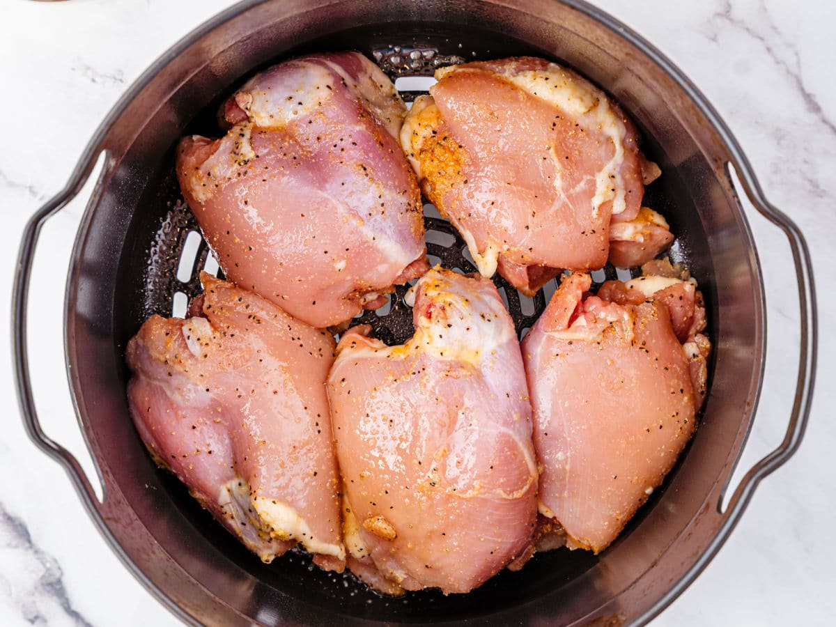 Five raw, seasoned Garlic Parmesan Chicken Air Fryer thighs arranged in a single layer inside an air fryer basket on a white marble surface.