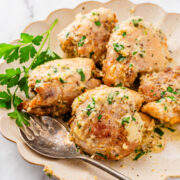 A plate of creamy Garlic Parmesan Chicken Air Fryer thighs garnished with chopped parsley, with a serving fork and a sprig of fresh parsley on the side.
