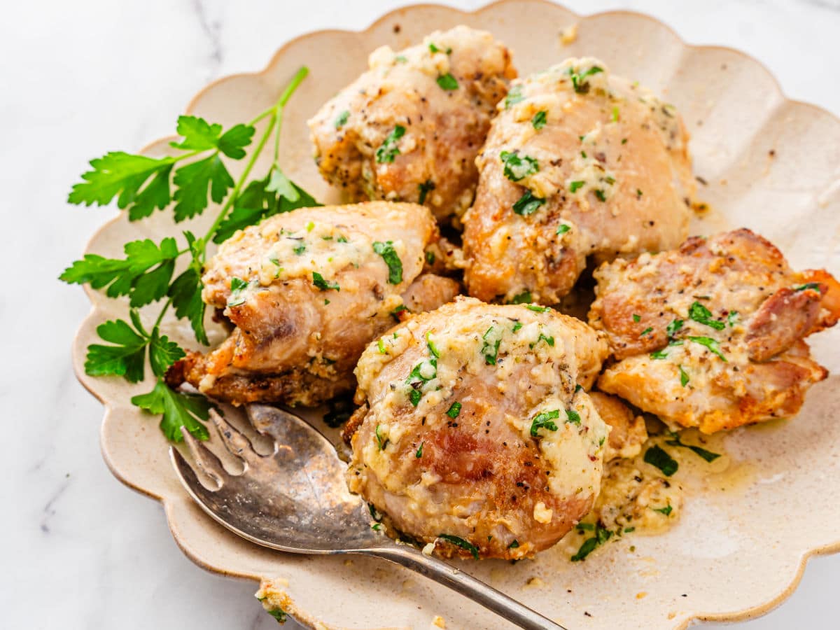 A plate of creamy Garlic Parmesan Chicken Air Fryer thighs garnished with chopped parsley, with a serving fork and a sprig of fresh parsley on the side.