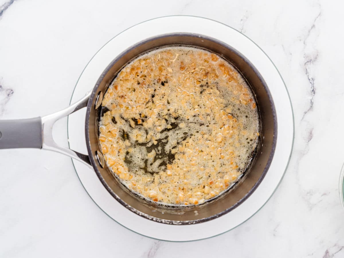 A saucepan with bubbling melted butter, showing golden brown specks, sits on a glass plate over a white marble surface—perfect for drizzling over Garlic Parmesan Chicken Air Fryer recipes.