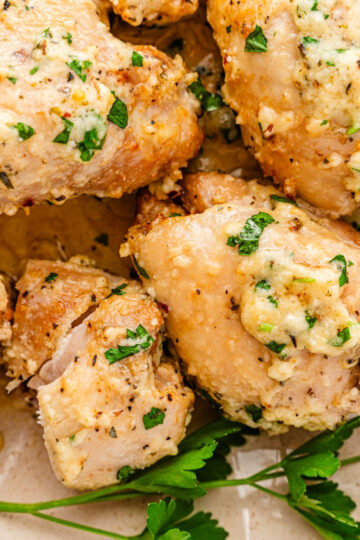 Close-up of Garlic Parmesan Chicken Air Fryer thighs topped with a creamy garlic and herb sauce, garnished with chopped parsley and served alongside fresh parsley sprigs.