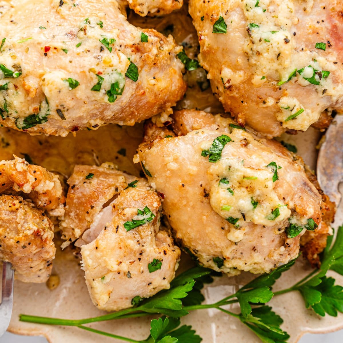 Close-up of Garlic Parmesan Chicken Air Fryer thighs topped with a creamy garlic and herb sauce, garnished with chopped parsley and served alongside fresh parsley sprigs.