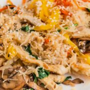 A plate of stir-fried rice noodles with sliced mushrooms, bell peppers, spinach, tofu strips, and sesame seeds, served on a white dish.