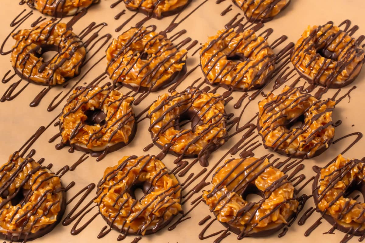 Rows of Somoa Copy Cat Cookies—round treats topped with caramel and coconut, drizzled and dipped in chocolate—are arranged neatly on parchment paper.