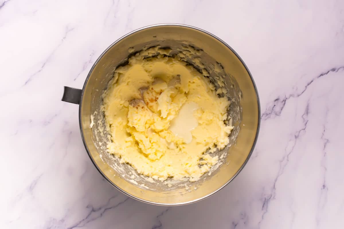 A metal mixing bowl with partially creamed butter and sugar sits on a white marble surface, ready for Somoa Copy Cat Cookies.