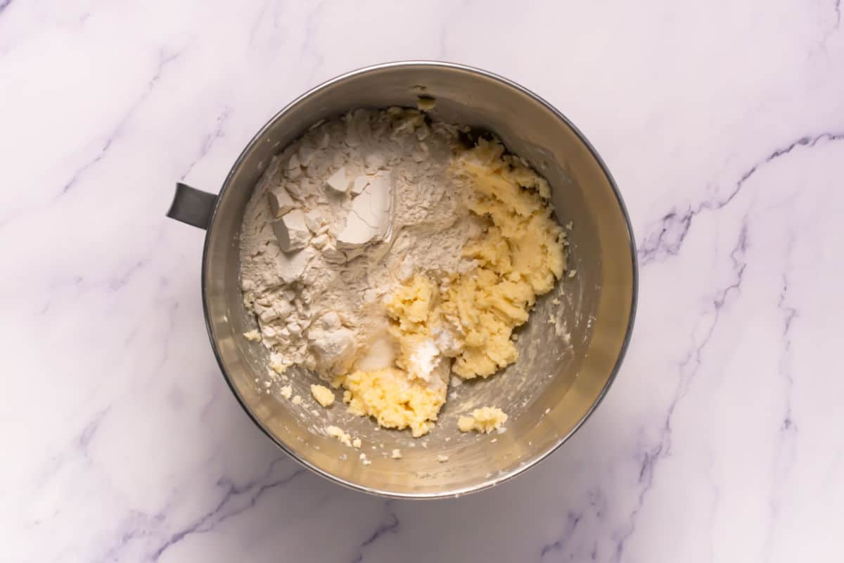 A metal mixing bowl containing partially mixed flour and creamed butter for Somoa Copy Cat Cookies sits on a white marble surface.