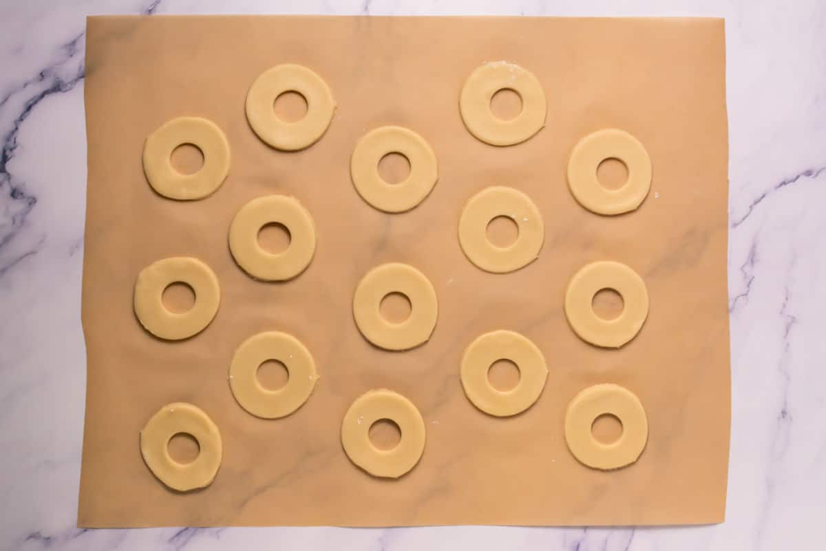 A sheet of parchment paper on a marble surface holds rows of Somoa Copy Cat Cookies, each round with a hole in the center, evenly spaced and ready for baking.
