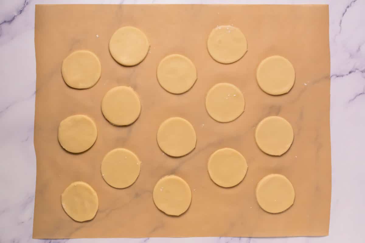Round Somoa Copy Cat Cookies dough shapes are evenly spaced on a sheet of parchment paper, ready for baking, with a marble surface underneath.