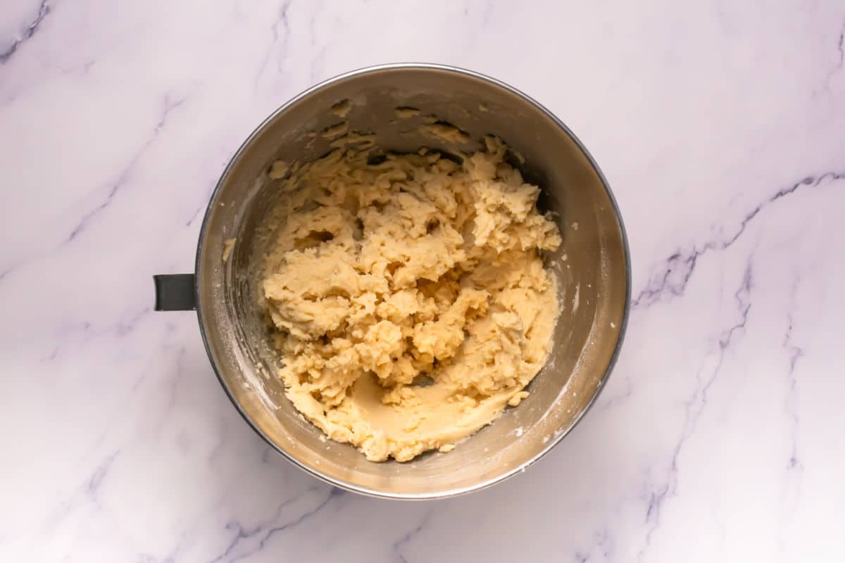 A metal mixing bowl filled with thick, creamy Somoa Copy Cat Cookies dough sits on a white marble countertop.
