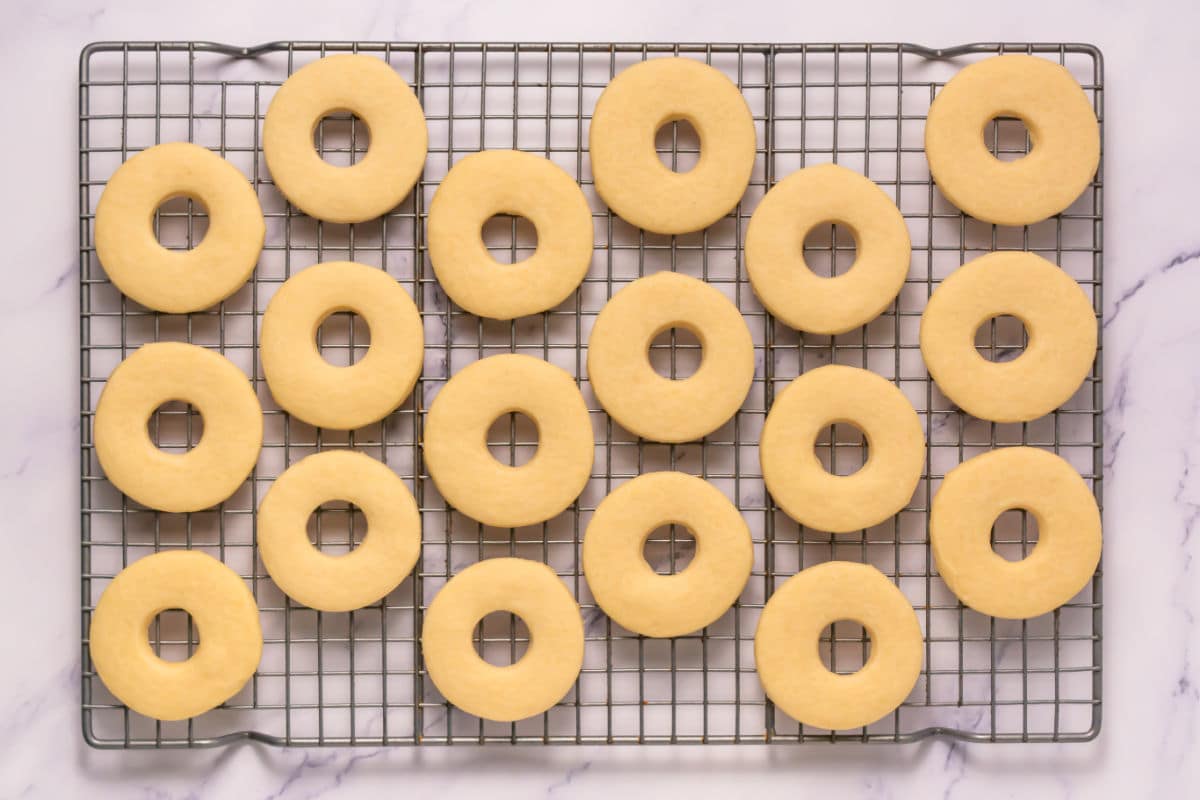 Somoa Copy Cat Cookies with holes in the center are arranged in neat rows on a metal cooling rack over a white marble surface. The cookies are pale and appear freshly baked.