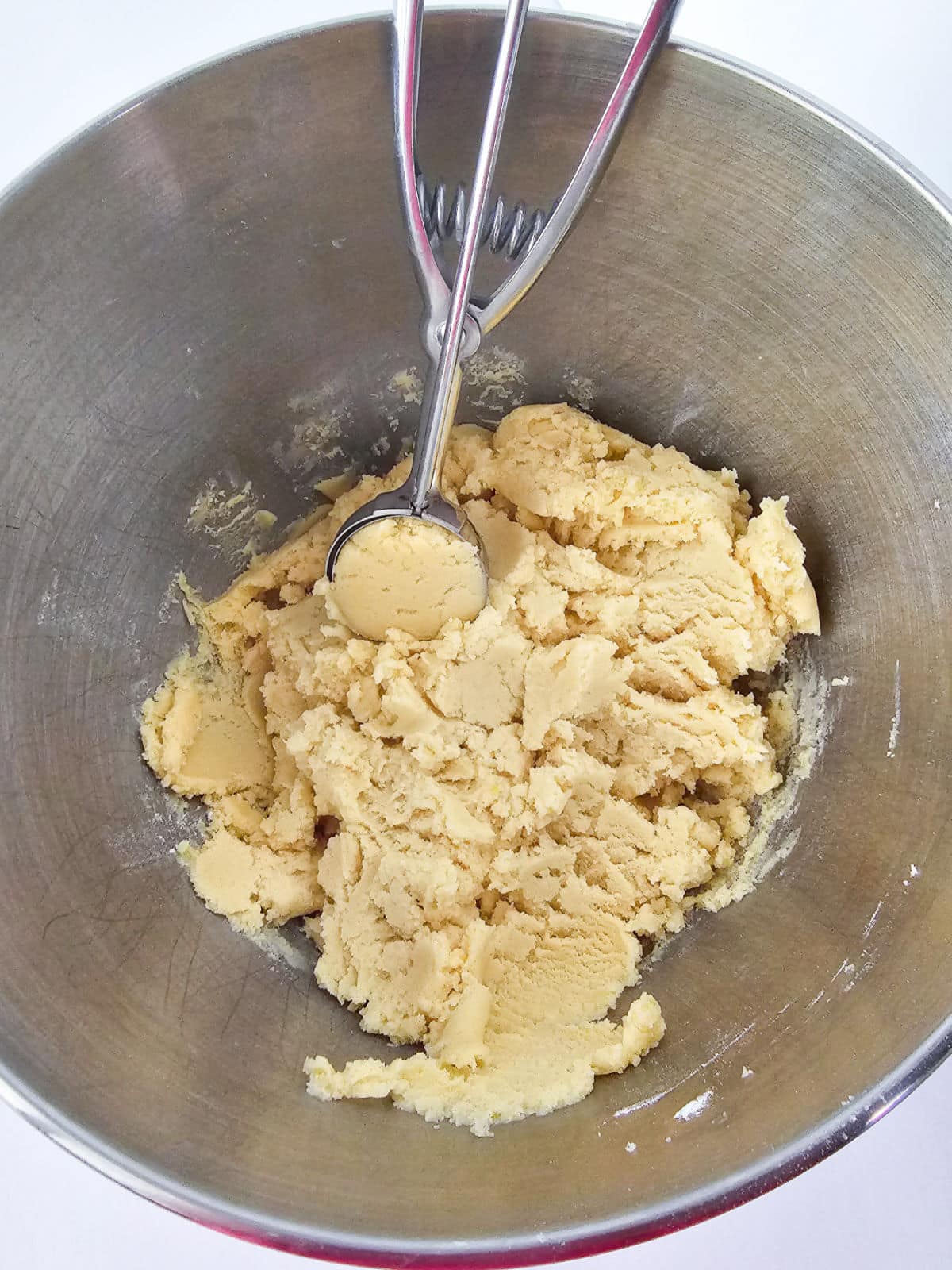 A metal mixing bowl filled with pale snickerdoodle cookie dough, with a metal cookie scoop resting on top of the dough.