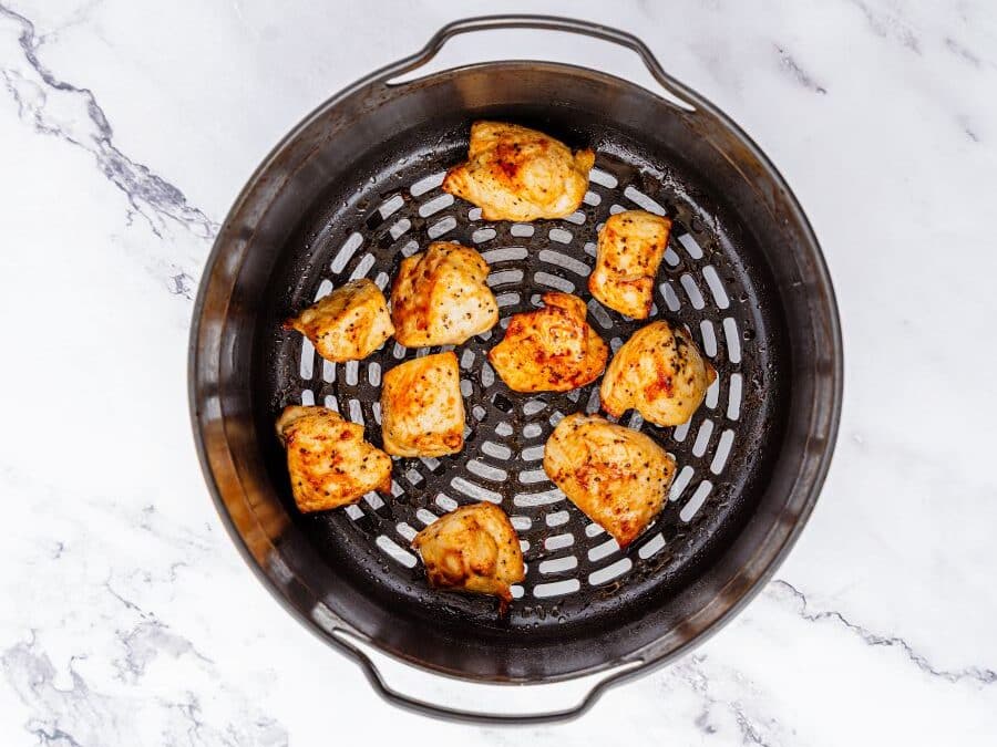Cooked, seasoned chicken nuggets arranged in a single layer inside the basket of an air fryer, ready to be paired with a honey garlic sauce, placed on a white marble surface.