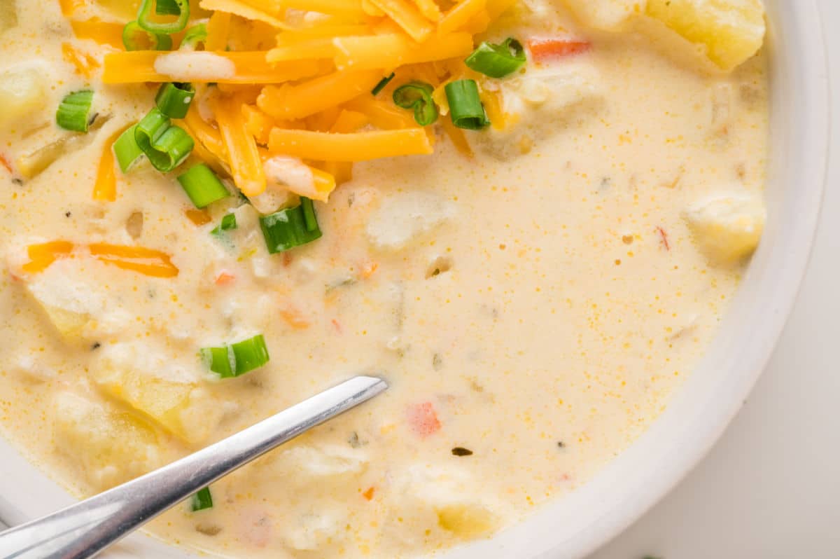 A close-up of creamy potato soup topped with shredded cheddar cheese and chopped green onions, with a spoon resting in the bowl. This comforting potato soup is perfect for chilly days.