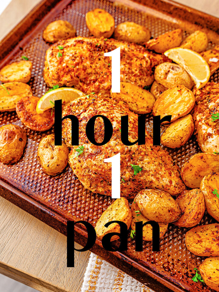 Sheet pan with seasoned chicken breasts, roasted baby potatoes, and lemon wedges. Overlaid text reads: 1 hour, 1 pan. Food rests on a kitchen towel, highlighting a simple sheet pan chicken and potatoes meal.