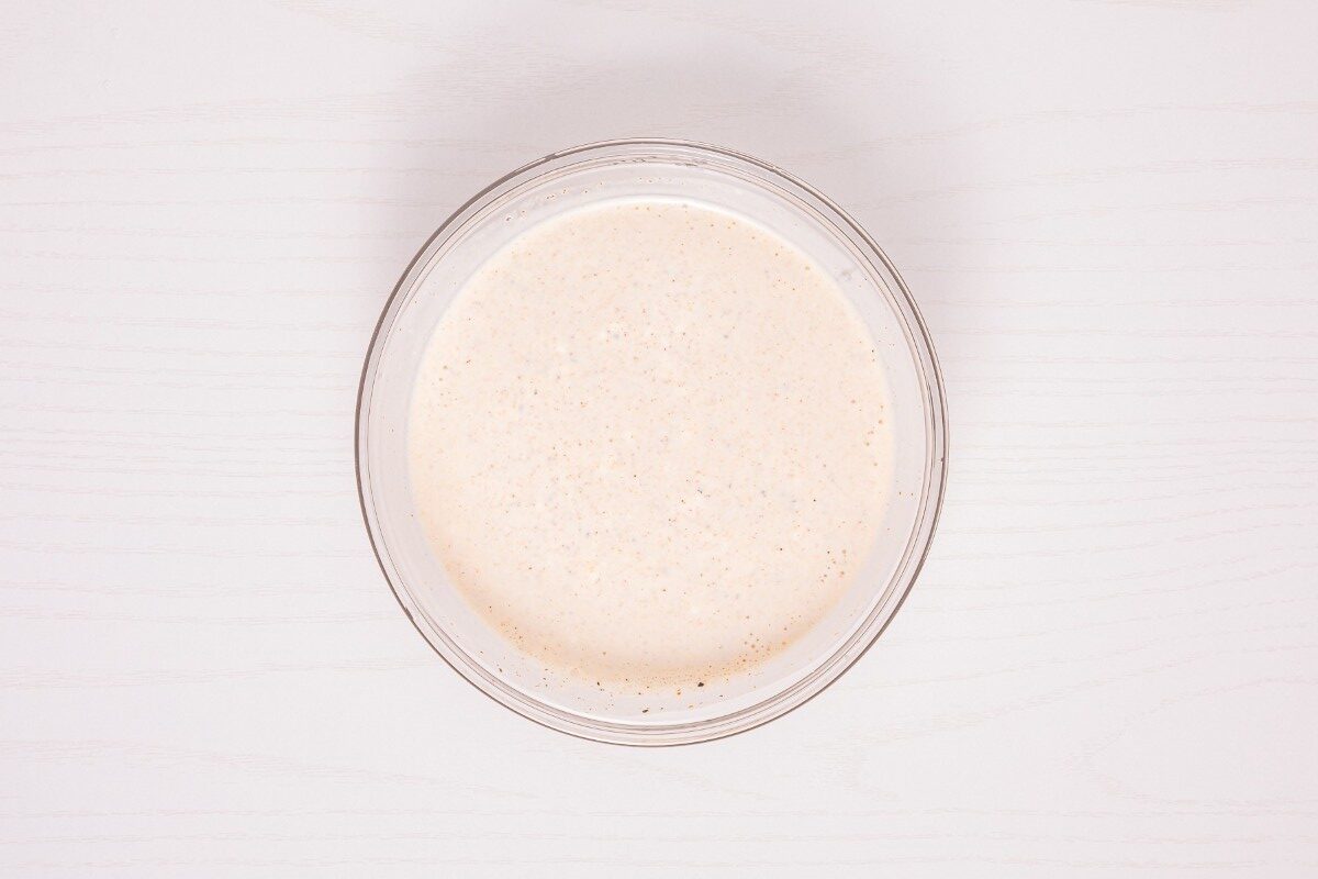 A clear glass bowl filled with a pale, creamy liquid sits on a light-colored wooden surface, viewed from above.