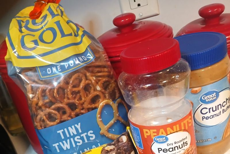 A bag of Rold Gold Tiny Twists pretzels for making almond bark pretzel candy, a jar of Great Value dry roasted peanuts, and a jar of Great Value crunchy peanut butter.