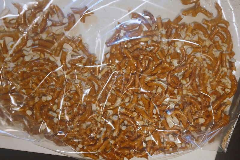 Broken almond bark pretzel sticks in a clear plastic bag.