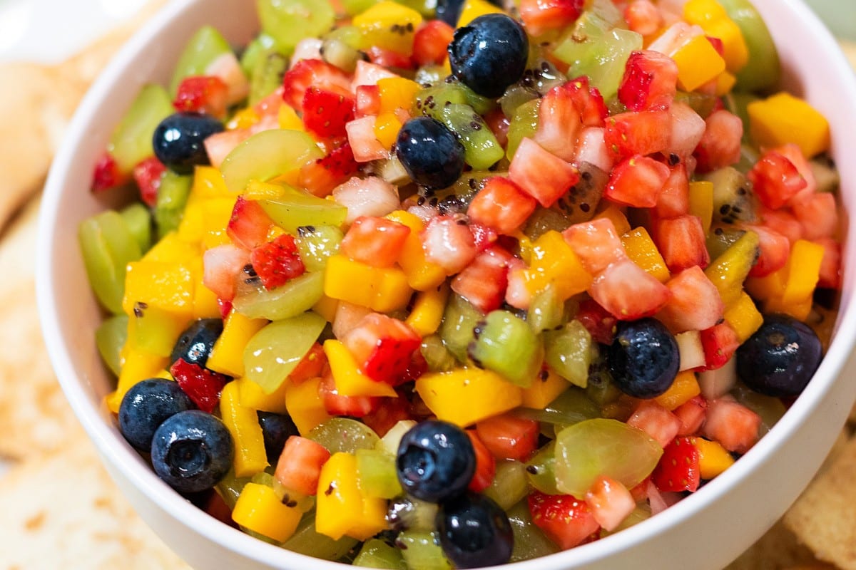 A white bowl filled with a fresh fruit salsa containing diced strawberries, mango, kiwi, and whole blueberries.