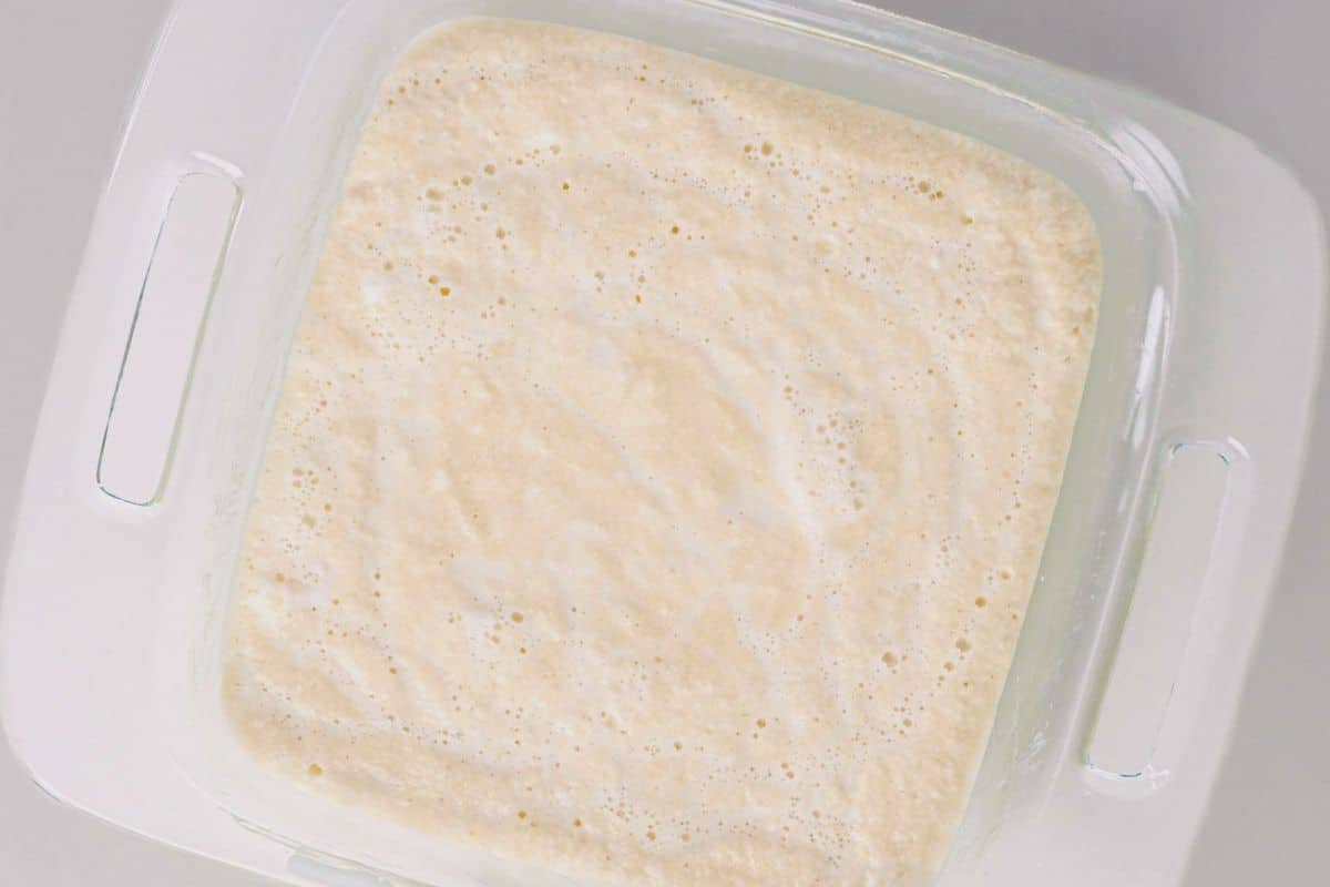 Light-colored batter for a cake that makes its own pudding in a square glass baking dish.